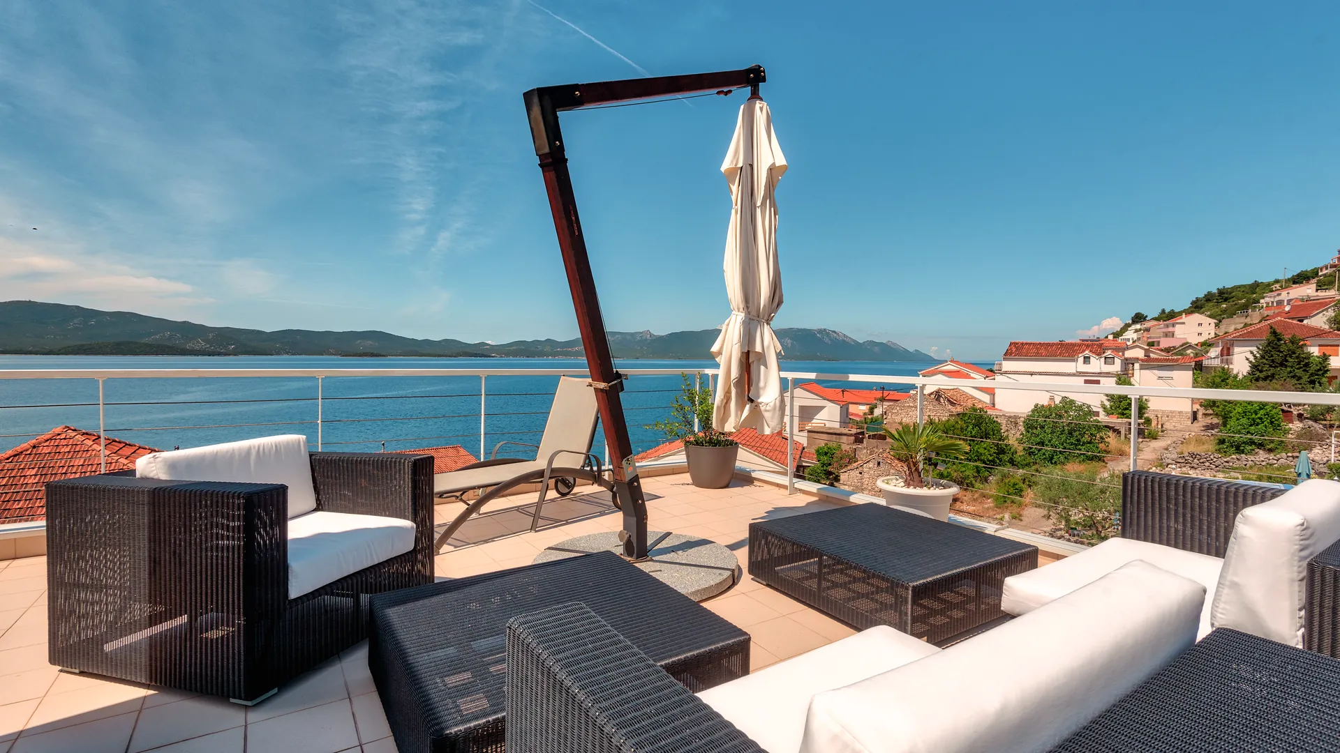 Střešní terasa s lounge nábytkem, lehátkem a výhledem na moře