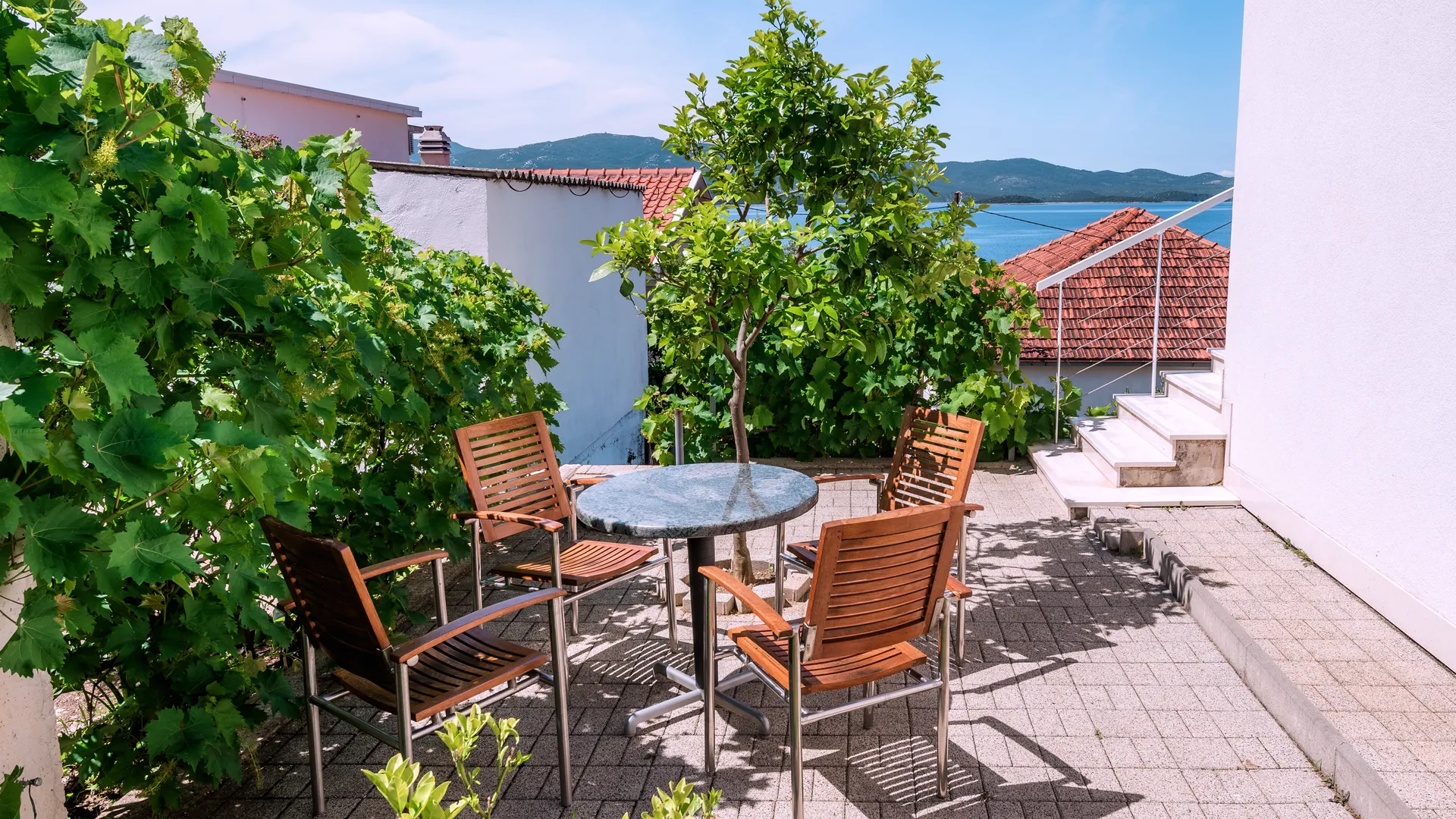 Gartenterrasse im Schatten einer Weinrebe mit Meerblick